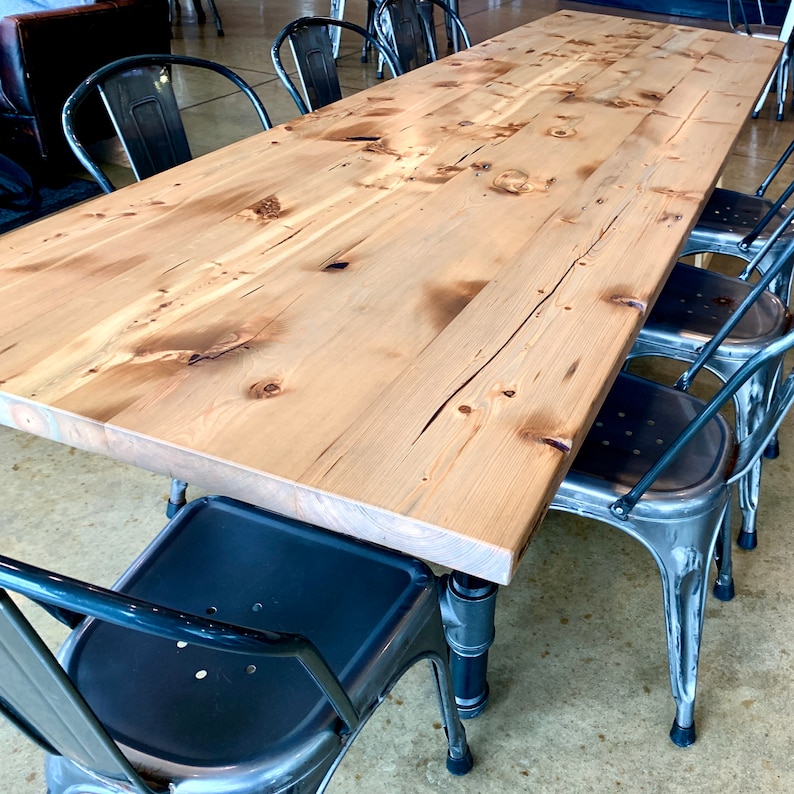 May include: A long, wooden table with a natural finish and a distressed look. The table is surrounded by black metal chairs with a distressed silver finish.