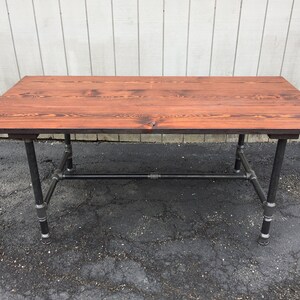 May include: A rustic wooden table with a dark brown stain finish, supported by a black metal pipe frame.