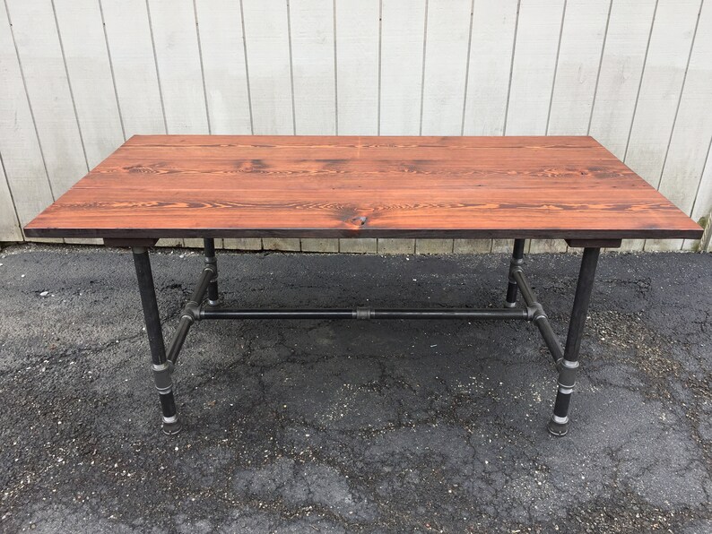 May include: A rustic wooden table with a dark brown stain finish, supported by a black metal pipe frame.