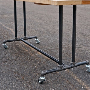 May include: A black metal table base with four wheels. The base is made of pipes and fittings. The table top is not visible in the image.
