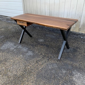 May include: A walnut wood desk with a single drawer and black metal X-shaped legs.