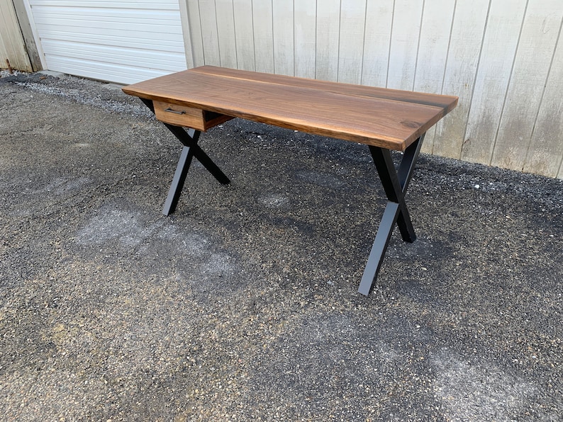 May include: A walnut wood desk with a single drawer and black metal X-shaped legs.