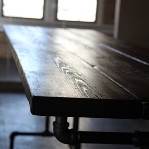 May include: A dark stained wooden table with a rectangular top and black metal pipe legs. The table's surface has visible wood grain and is supported by industrial-style plumbing pipes.