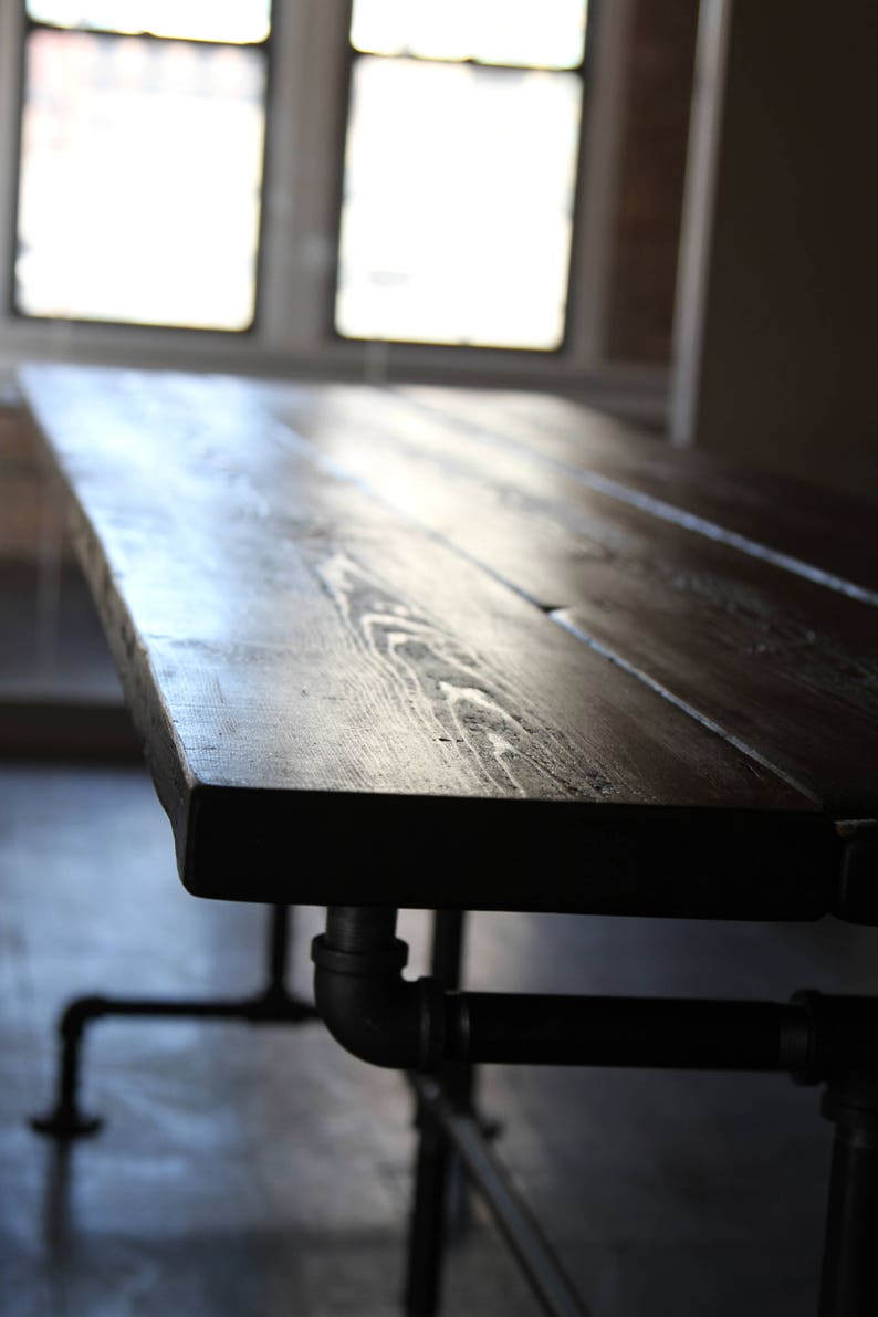 May include: A dark stained wooden table with a rectangular top and black metal pipe legs. The table's surface has visible wood grain and is supported by industrial-style plumbing pipes.