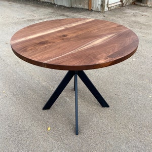 May include: A round wooden table with a dark brown walnut top and a black metal tripod base.