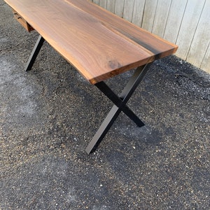 May include: A dark brown wooden desk with a live edge top and a single drawer. The desk has black metal X-shaped legs.