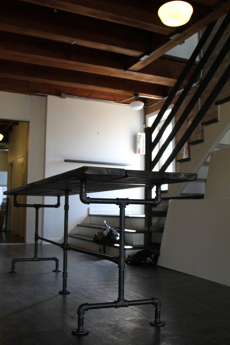 May include: A dark wood table with a black pipe frame. The table has a rectangular top and is supported by a network of black pipes and fittings. The table is approximately 72 inches long and 36 inches wide.