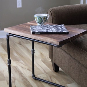 May include: A wooden table with a black metal frame. The table is next to a brown couch and has a book and a cup of coffee on it. The book is titled "Lost Chicago" by David Garrad Lowe.