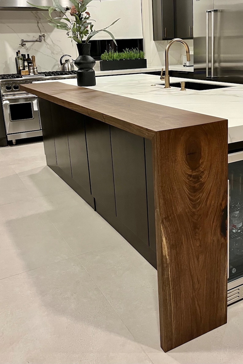 May include: A kitchen island featuring a dark brown natural wood waterfall countertop with visible grain patterns. The base of the island consists of matte black cabinetry panels. The countertop extends vertically to the floor on one side.