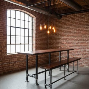 May include: A dark wood dining table and bench set with black pipe legs. The table is 183 cm long and the bench is 152 cm long. The set is in a room with a brick wall and a large window.