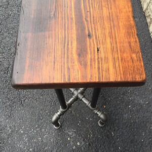 May include: A small wooden table with a rustic, brown wood top and a black metal pipe base.