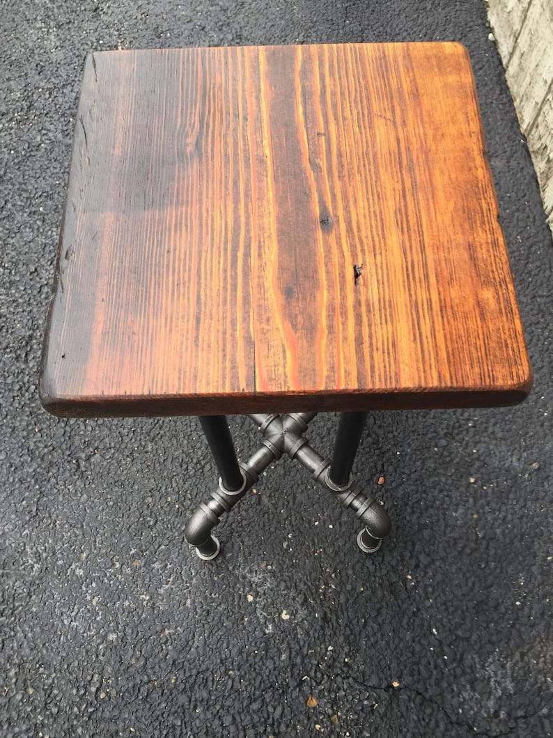 May include: A small wooden table with a rustic, brown wood top and a black metal pipe base.