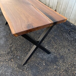 May include: A wooden table top with a live edge and a natural wood finish. The table has black metal legs in an X shape.