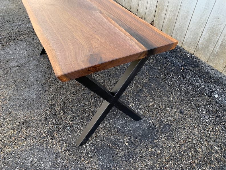 May include: A wooden table top with a live edge and a natural wood finish. The table has black metal legs in an X shape.