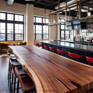 May include: A long live-edge wooden bar table with a dark brown grain and natural irregular edges, paired with several dark wooden bar stools. The setting includes a black bar counter with red stools, large windows, and a metal ceiling structure.