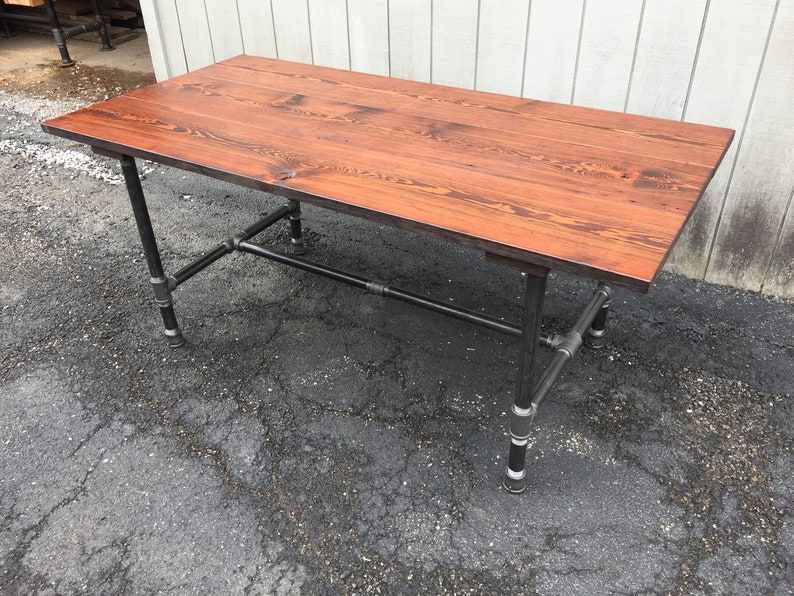 May include: A rectangular wooden desk with a reddish-brown finish. The tabletop is supported by black metal pipes and fittings, creating an industrial aesthetic. The desk is approximately 152 cm long.