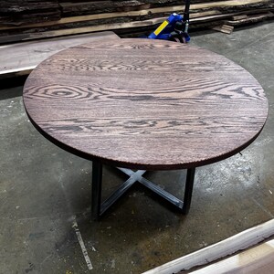 May include: A round, dark brown wooden table with a distinctive grain pattern. The table has a metal X-shaped base. The table is approximately 76 cm in diameter.