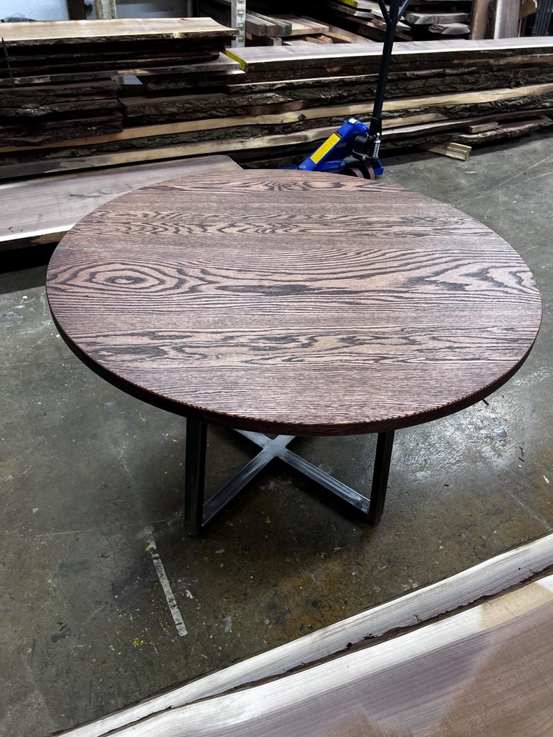 May include: A round, dark brown wooden table with a distinctive grain pattern. The table has a metal X-shaped base. The table is approximately 76 cm in diameter.