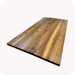 May include: A rectangular wooden tabletop with a natural wood grain pattern. The wood has a warm, brown color with variations in tone, and a dark edge. The surface is smooth and appears to be finished with a clear coat.