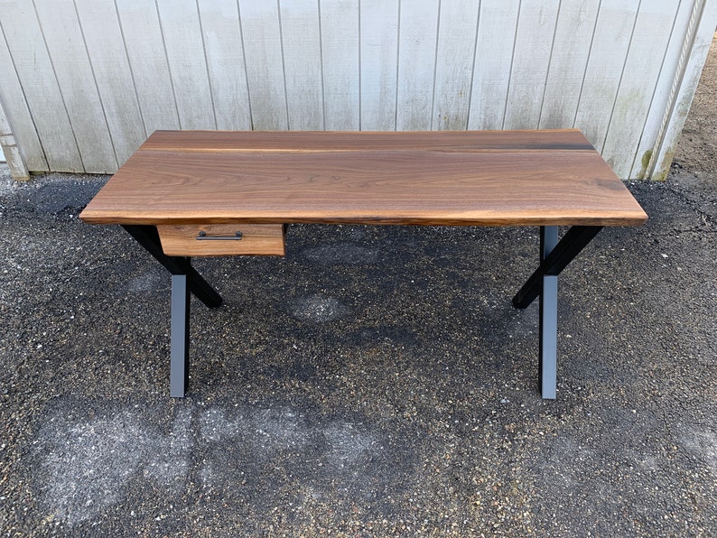 May include: A walnut wood desk with a single drawer and black metal legs. The desk has a live edge design and a natural wood finish.