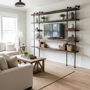 May include: A wall-mounted shelving unit constructed from dark brown wooden planks and black metal industrial pipes. The unit features five horizontal shelves arranged around a central television, with various decorative items and baskets.