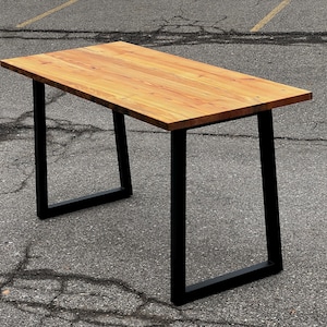 May include: A rectangular wooden table with a light brown surface and black metal legs. The table is approximately 152 cm long and 76 cm wide, with a simple, modern design. The legs are a square shape.