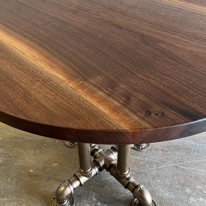 May include: A round wooden table with a dark brown finish. The tabletop is supported by a metal pipe base with a silver finish. The table has a diameter of approximately 36 inches.