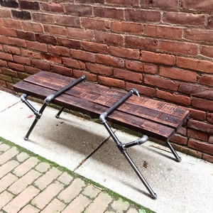 May include: A rustic wooden bench with black metal pipe legs. The bench is made of reclaimed wood and has a natural finish. The legs are made of industrial pipe and have a black powder coat finish.