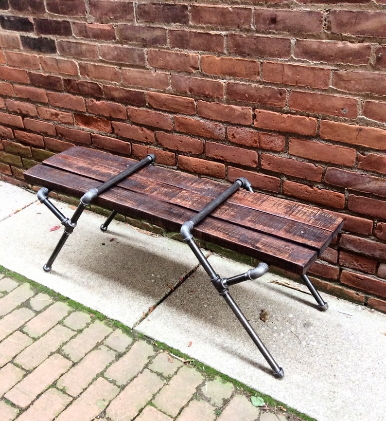 May include: A rustic wooden bench with black metal pipe legs. The bench is made of reclaimed wood and has a natural finish. The legs are made of industrial pipe and have a black powder coat finish.