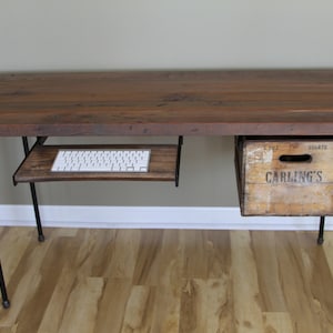 May include: A rustic wooden desk with black metal pipe legs. The desk has a pull-out keyboard tray and a wooden drawer with the text "Carling's" printed on it.