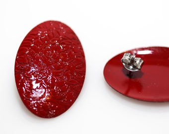May include: A pair of red oval-shaped earrings with a textured surface. One earring has a silver post and back.