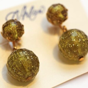 May include: A pair of gold tone dangle earrings with two green glass beads on each earring. The beads are faceted and have a sparkly finish.