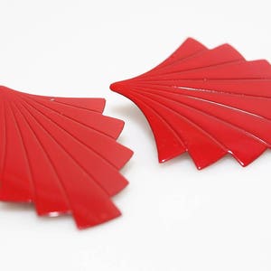 May include: A pair of red, fan-shaped earrings. The earrings are made of metal and have a shiny finish.