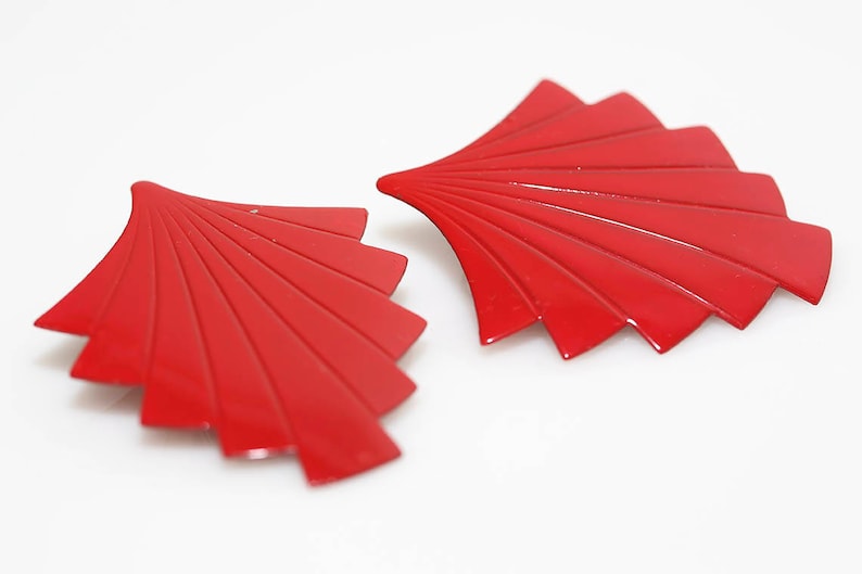 May include: A pair of red, fan-shaped earrings. The earrings are made of metal and have a shiny finish.