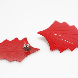 May include: A pair of red fan-shaped earrings with silver posts. The earrings are made of metal and have a glossy finish.