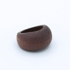 May include: A dark brown wooden ring with a smooth, rounded surface. The ring is made of a single piece of wood and has a natural, organic look.