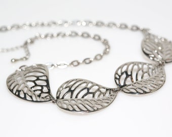 May include: A silver necklace with a chain and three leaf-shaped pendants. The leaves are openwork and have a delicate design.