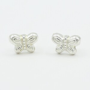 May include: A pair of silver-colored butterfly stud earrings. Each earring features a detailed butterfly design with rounded wings and a textured surface. The earrings are displayed on a white background.
