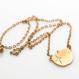 May include: A gold chain necklace with a gold apple pendant. The apple has a star design.