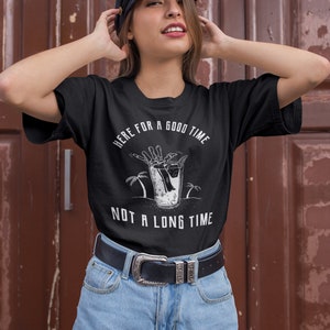 May include: Black t-shirt with a white graphic of a skeleton hand reaching into a glass of liquid with palm trees in the background. The text "Here for a good time not a long time" is printed on the shirt.