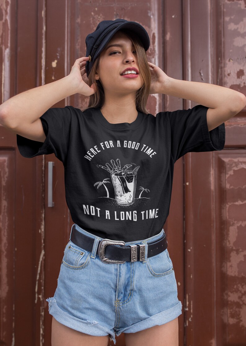 May include: Black t-shirt with a white graphic of a skeleton hand reaching into a glass of liquid with palm trees in the background. The text "Here for a good time not a long time" is printed on the shirt.