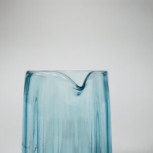 May include: A light blue glass pitcher with a textured, wavy design. The pitcher has a wide mouth and a rounded base.