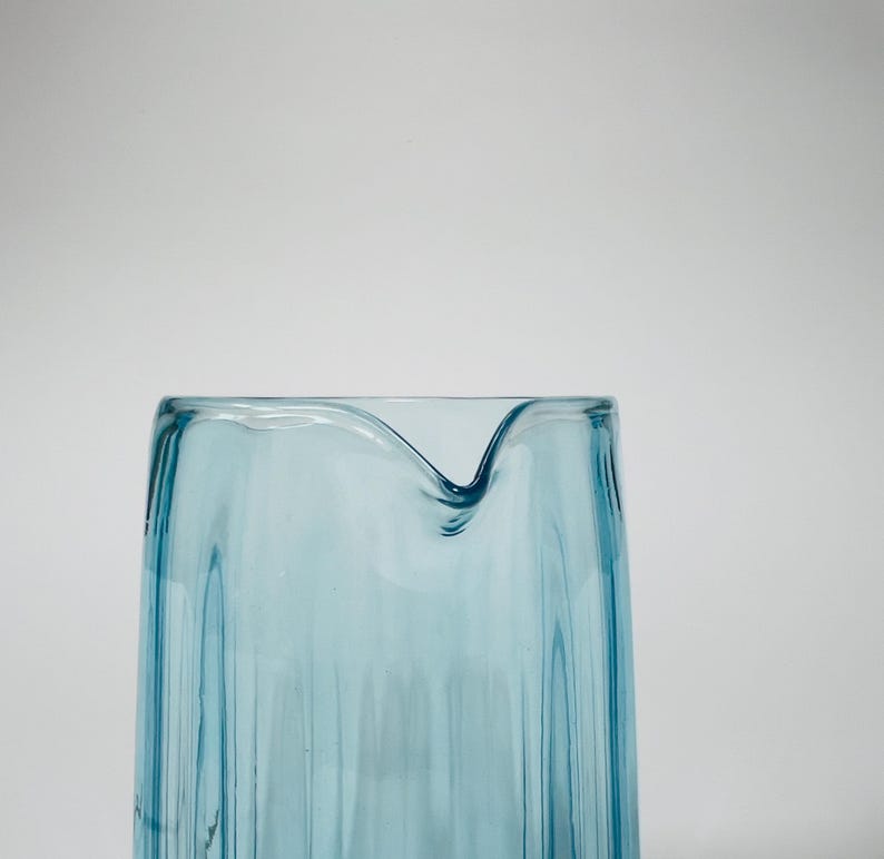 May include: A light blue glass pitcher with a textured, wavy design. The pitcher has a wide mouth and a rounded base.
