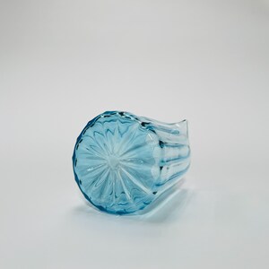 May include: A light blue glass pitcher with a textured, starburst pattern on the bottom. The pitcher has a wide mouth and a handle.