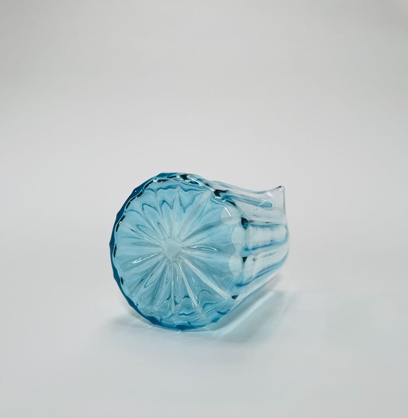 May include: A light blue glass pitcher with a textured, starburst pattern on the bottom. The pitcher has a wide mouth and a handle.