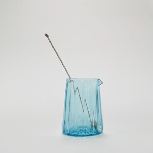 May include: A light blue glass pitcher with a textured surface and a silver stirring spoon inside.