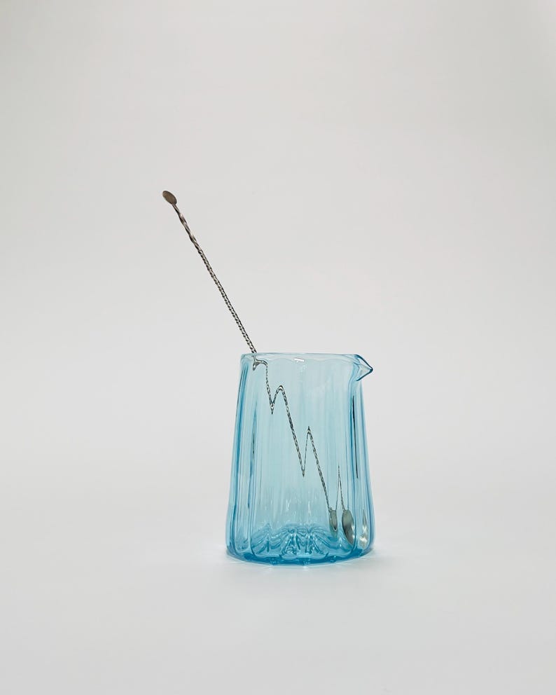 May include: A light blue glass pitcher with a textured surface and a silver stirring spoon inside.