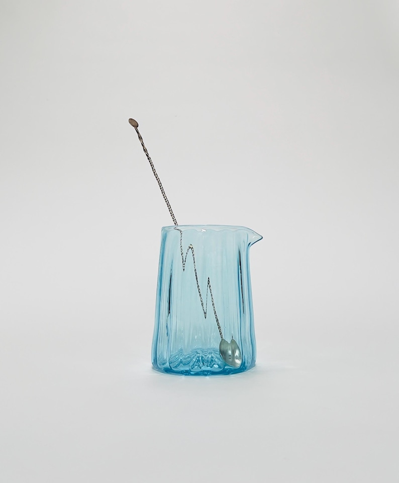 May include: A light blue glass pitcher with a textured surface and a silver stirring spoon inside.