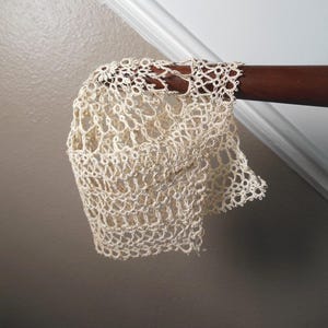 May include: A delicate, off-white crocheted lace doily with a floral pattern. The doily is draped over a wooden surface.