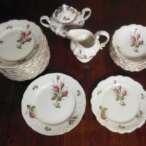 May include: A set of white porcelain dinnerware with a delicate floral design. The set includes a sugar bowl with lid, creamer, and a stack of plates.